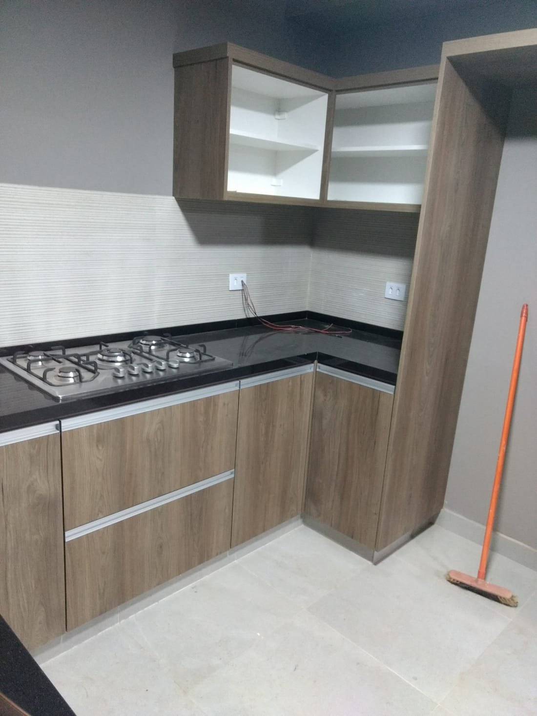 Cozinha planejada em L com cooktop e acabamento amadeirado, projeto da Prado Marcenaria